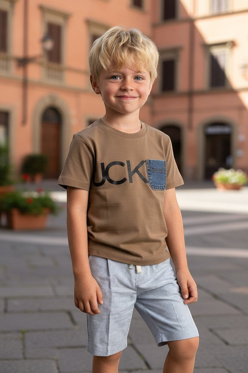 Bambino biondo indossa una t-shirt marrone Scugnizzi 0-16 con stampa grafica e taschino in denim in una piazza