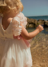 Abito da cerimonia Scugnizzi bianco e rosa in tulle con pizzo floreale, maniche a volant e cintura in raso.