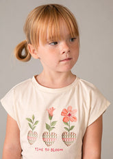 Bambina con maglietta color crema Scugnizzi 0-16 con stampa floreale "Time to Bloom" e pantaloni coordinati con stampa geometrica.
