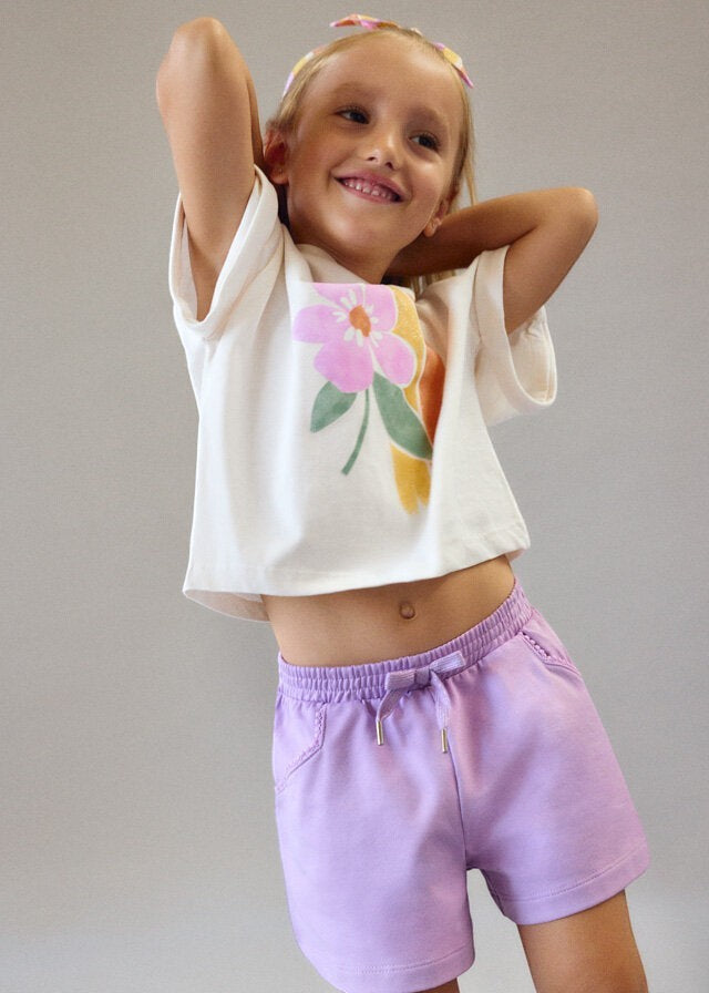 Bambina indossa completo Scugnizzi 0-16 con maglietta bianca a stampa floreale e pantaloncini lilla in cotone