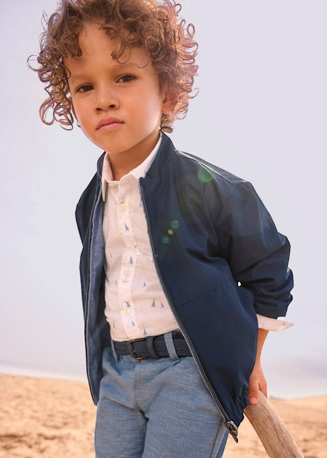 Bambino indossa giacca bomber reversibile blu Scugnizzi 0-16 con camicia bianca e pantaloni azzurri in spiaggia