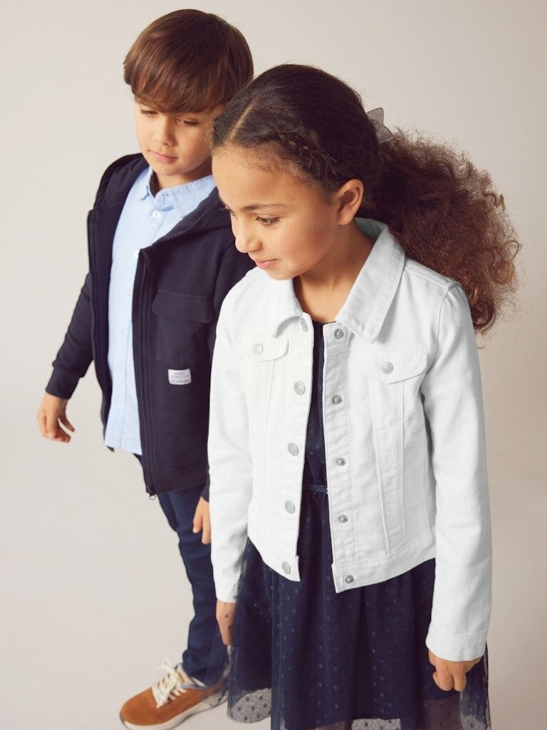 Bambina indossa giacca in denim bianca Scugnizzi 0-16 con bottoni metallici sopra un vestito blu scuro