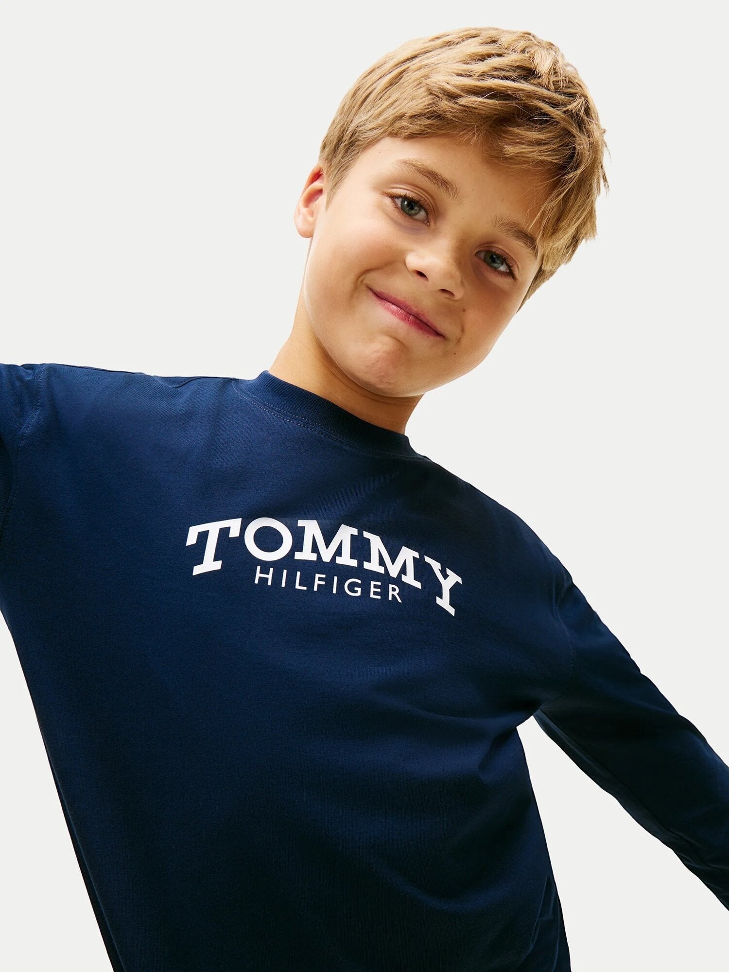 Ragazzo indossa maglia a maniche lunghe blu Tommy Hilfiger con logo bianco sul petto, proposta da Scugnizzi 0-16