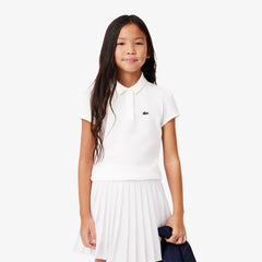 Bambina indossa polo bianca Lacoste Scugnizzi 0-16 in piqué di cotone con colletto smerlato e maniche arricciate.