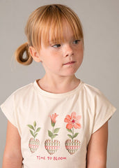 Bambina con maglietta color crema Scugnizzi 0-16 con stampa floreale "Time to Bloom" e pantaloni coordinati con stampa geometrica.
